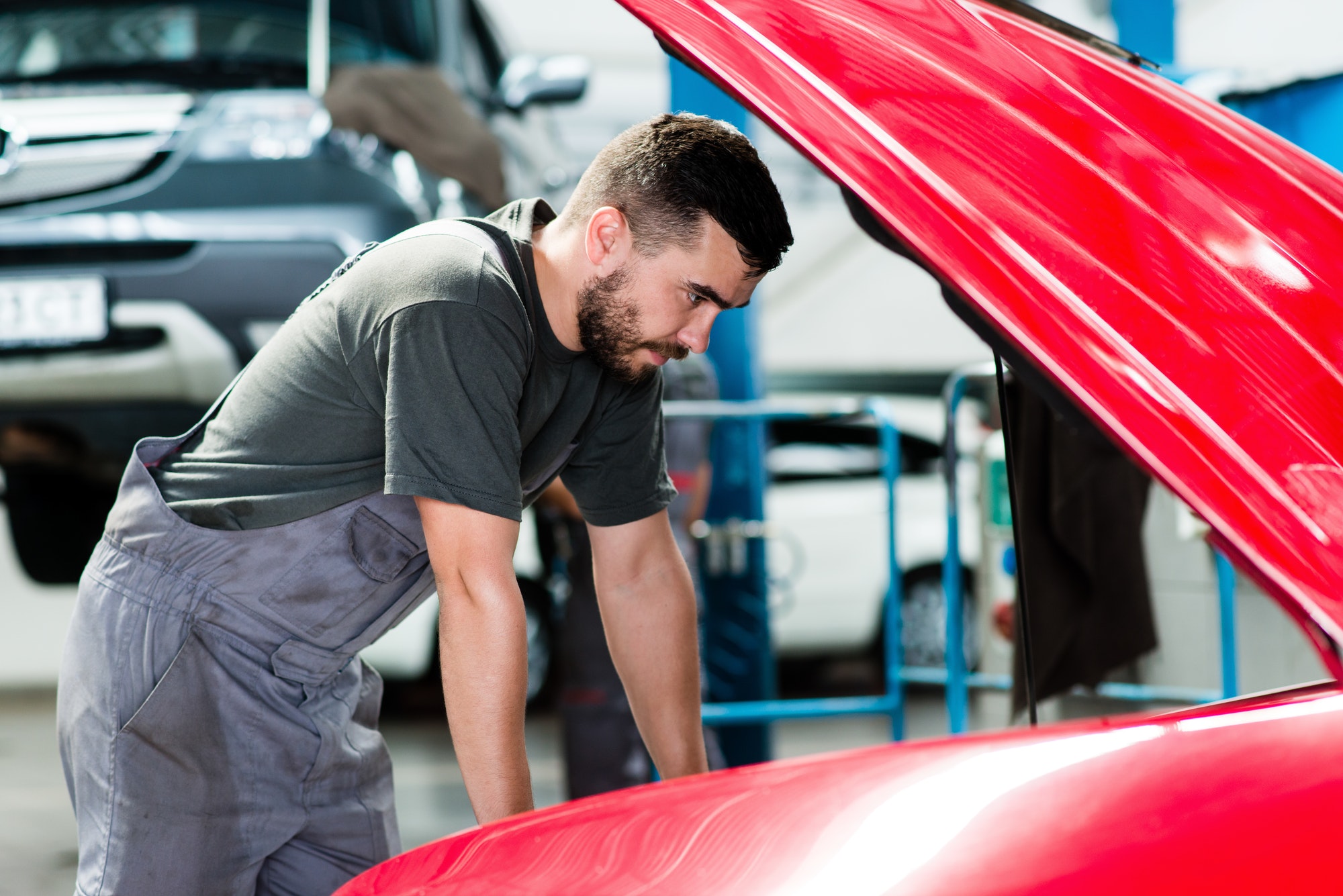 Auto mechanic working in garage. Repair service looking at the car's motor. - Image