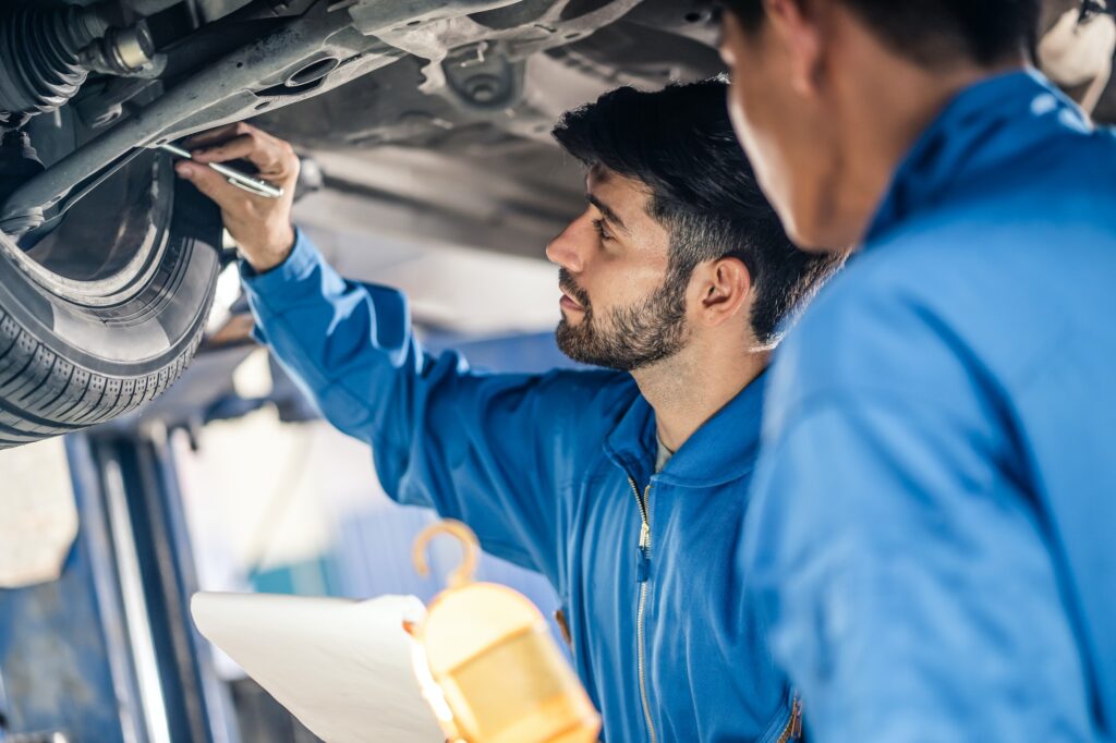 Vehicle service maintenance handsome mens checking under car condition in garage.